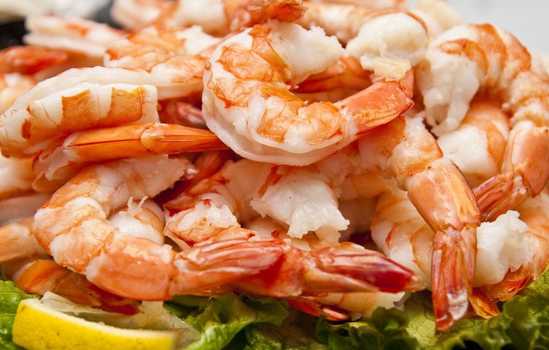 This photo shows pink boiled shrimp with lettuce and lemon slices on a plate.