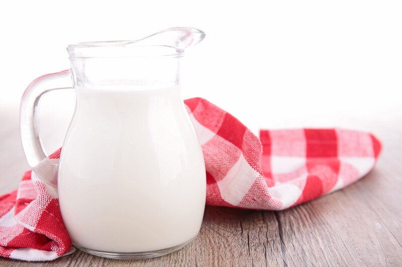 on a wooden surface is a clear jug of skim milk with a red and white table napkin at the back