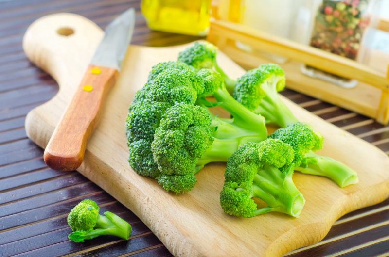 fresh broccoli florets and a small knife on top of a wood chopping board