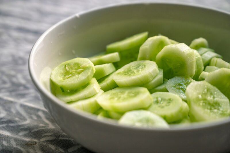 a closeup image of a ceramic light beige bowl with sliced cucumber