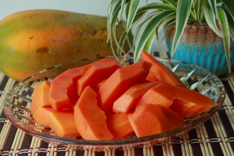 a whole papaya and sliced papaya on a clear glass plate
