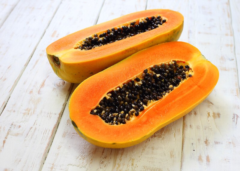 sliced papaya | Food For Net on a white wooden surface is a fresh papaya cut in half exposing its yellow flesh and black seeds
