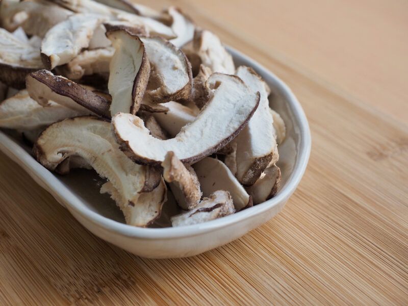 on a wooden surface is a white elongated dish  with sliced shiitake mushrooms