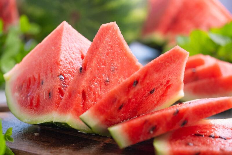 a closeup image of slices of watermelon on a wooden surface with herbs and more sliced watermelon at the back