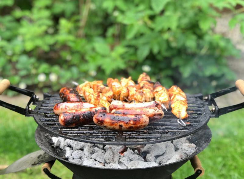 small backyard grill with sausages and chicken cubes on skewers