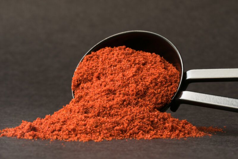 on a dark surface and dark background is a metal scoop with smoked paprika, resting on its side on a small mound of smoked paprika