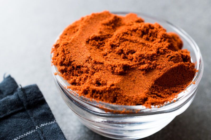 on a concrete surface is a clear glass bowl full of smoked paprika with a partial image of blue table napkin beside it