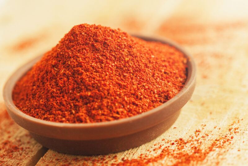 on a wooden surface is a clay bowl full of smoked paprika with loose smoke paprika powder around it