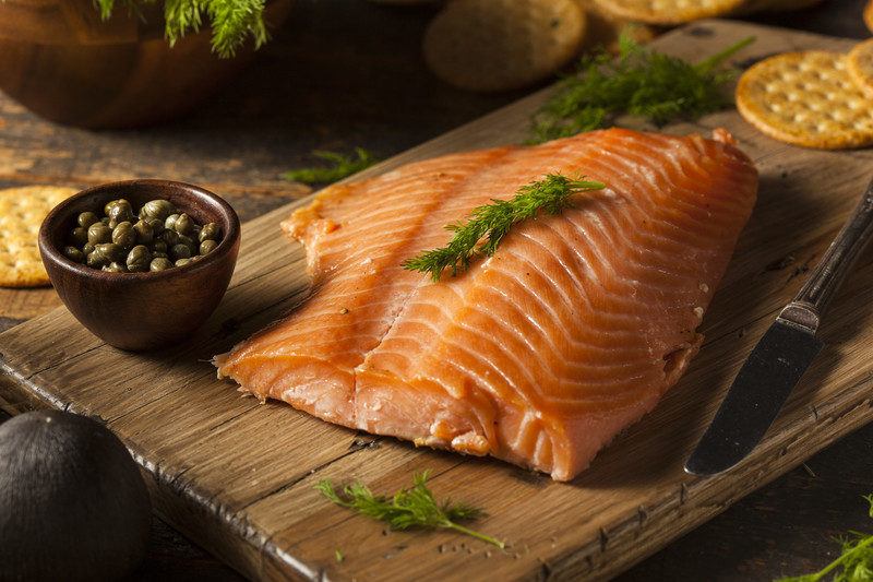 smoked salmon on a wooden block with capers, crackers, and dill you could receive in a smoked salmon of the month club