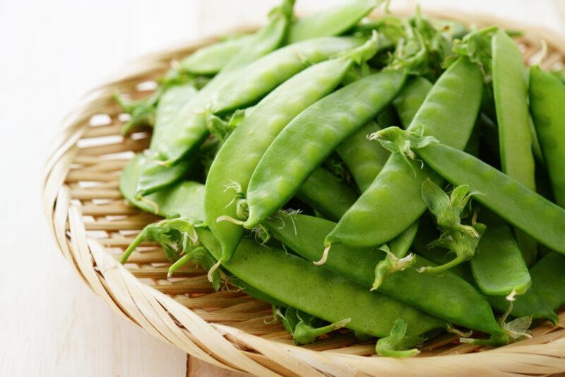 on a wooden surface is a weaved tray with snow peas