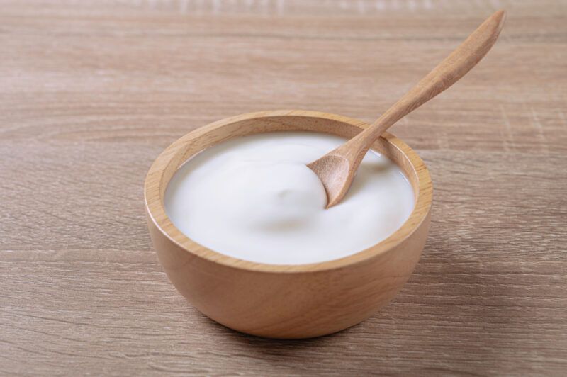 on a wooden surface is a wooden bowl of sour cream with a wooden spoon in it