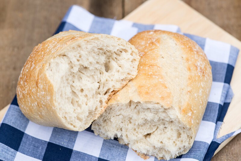 sourdough bread torn in half, resting on top of a white and blue kitchen towel on a wooden board