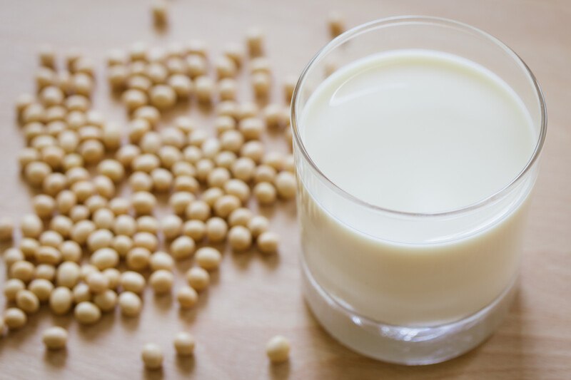 on a wooden surface is a glass of soy milk with loose soy milk  around it