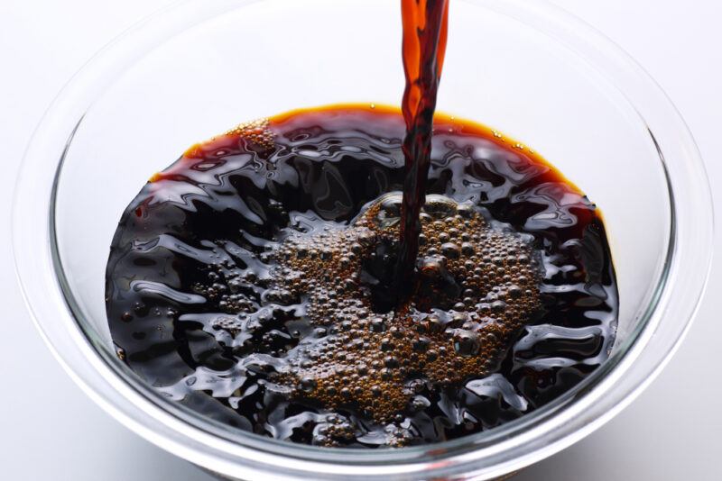 a closeup image of a clear glass bowl with soy sauce being poured into it