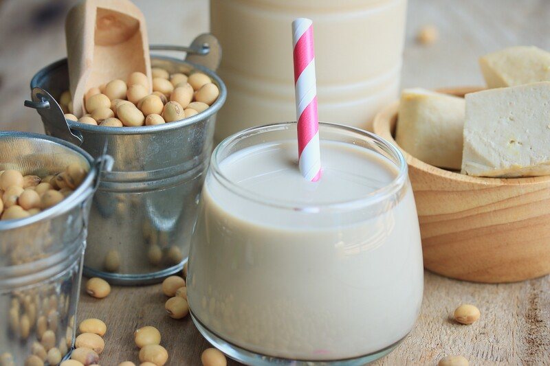 a glass of milk of soya mil with white and pink straw, a couple of little metal buckets full of soya, and a bowl of tofu