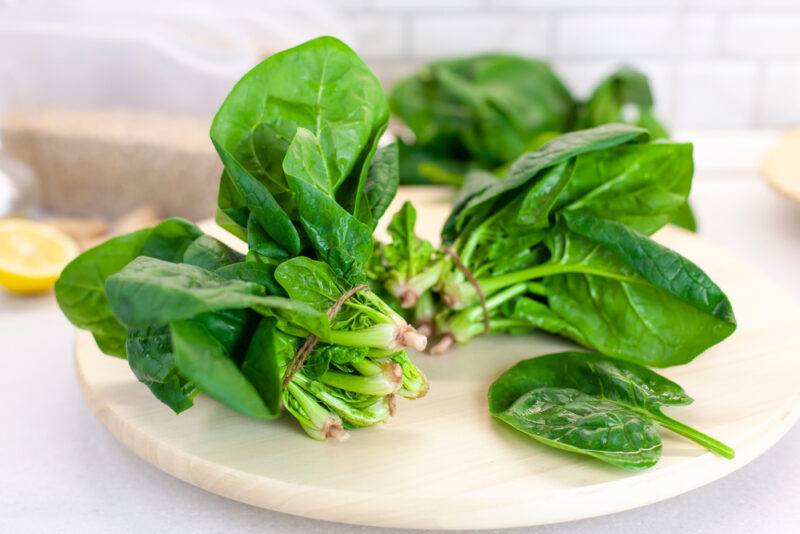 on a white surface is white wooden round chopping board  with bunches of spinach on it