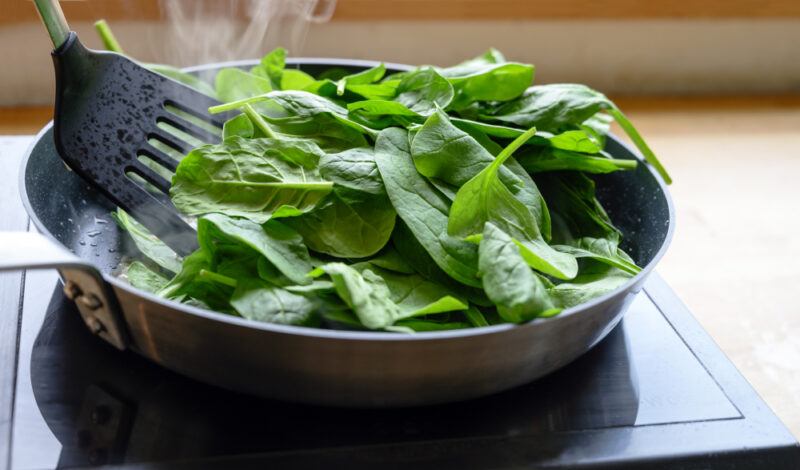 a frying pan with fresh spinach over a an electric stove