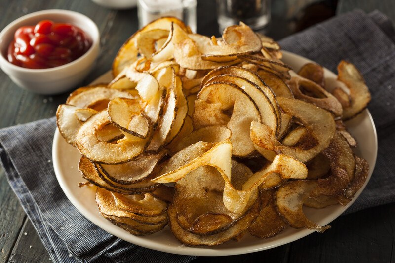 on a dark bluish table napkin is a dish full of spiral potato fries, with a small dish with red dipping sauce at the back