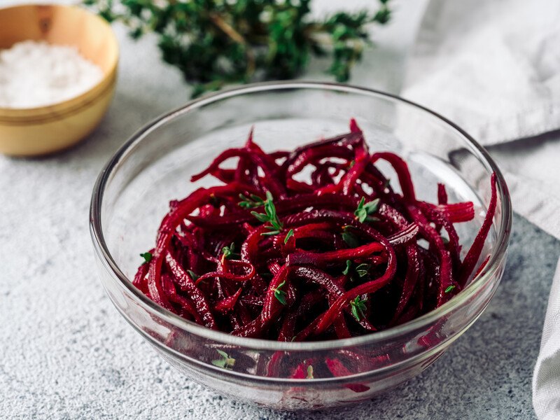 clear glass bowl of spiralized beets, with a small dish of salt and herbs at the back