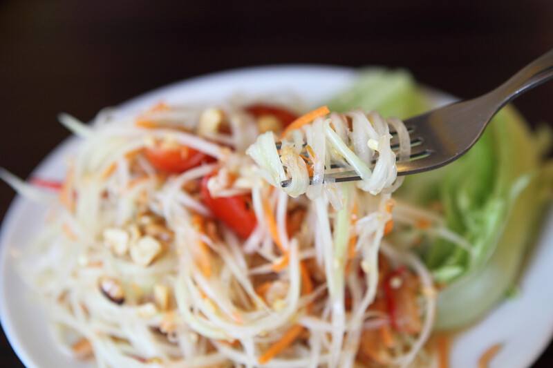 a closeup shot of spiralized green papaya salad with focus on the fork with salad