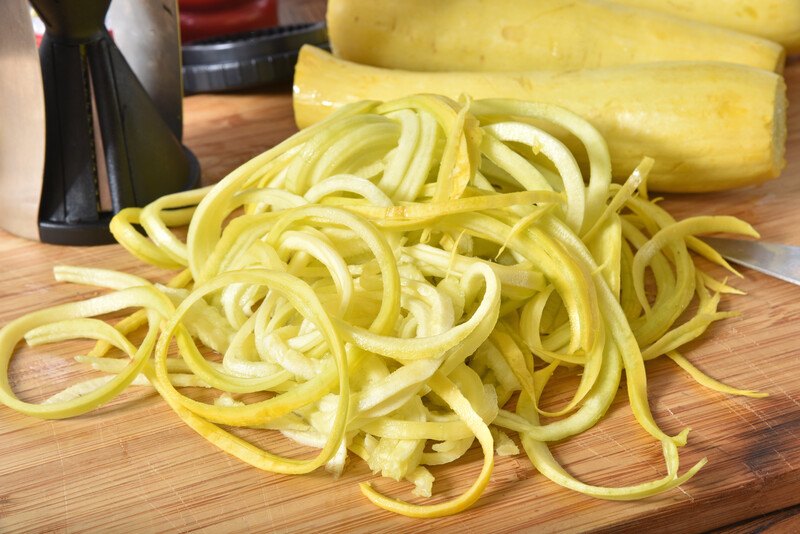 closeup shot of a spiralized yellow squash on a wooden chopping board, with whole yellow squash at the back