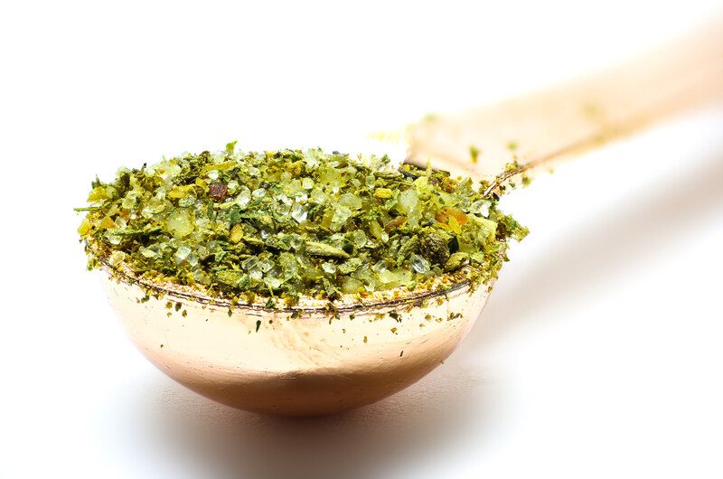 a metal measuring spoon full of Italian seasoning against a white background