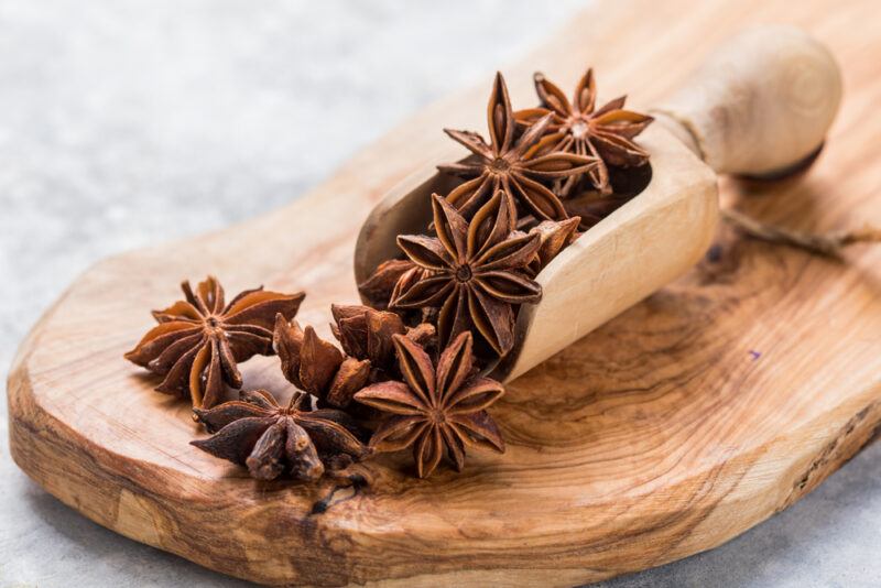 on a wooden chopping board are star anise with a wooden scoop full of star anise, too