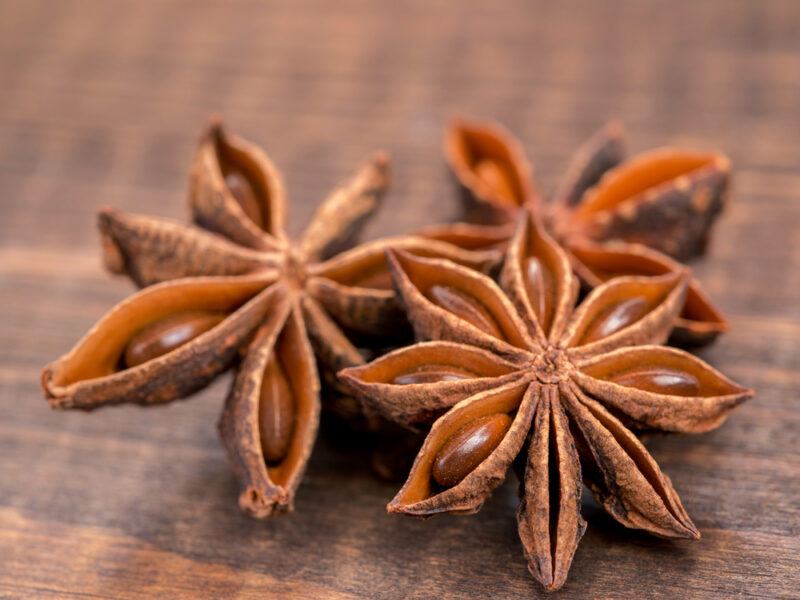 on brown wooden surface is a closeup image of three star anise