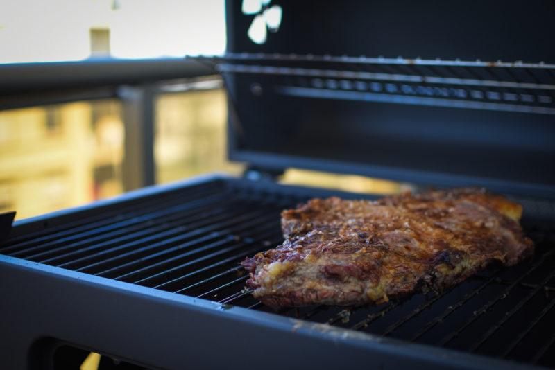 steak with seasoning beign grilled on gas grill on metal balcony