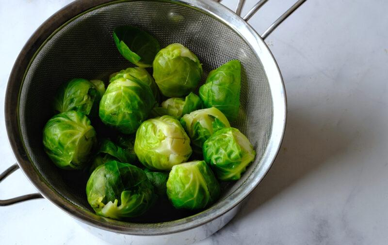 on a marble surface are steamed Brussels sprouts still in a metal colander