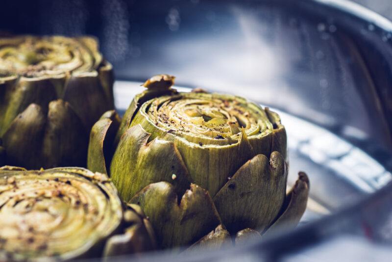 a closeup image of steamed artichokes still in a metal steaming basket