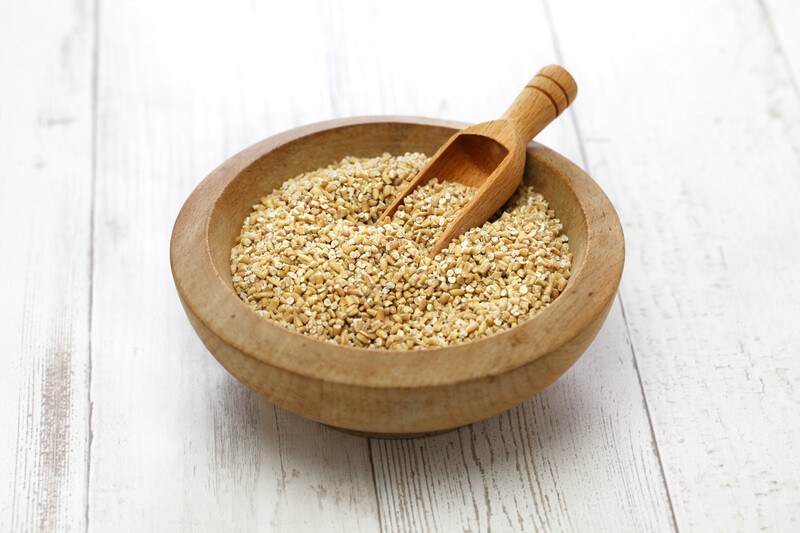 on a white rustic wooden surface is a thick wooden bowl with steel-cut oat with a wooden scoop shoved in it