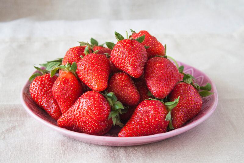 on a white table cloth is a pink glass plate with strawberries