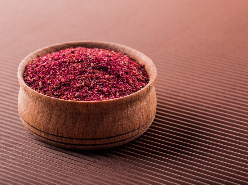 on a red surface is a wooden bowl full of sumac