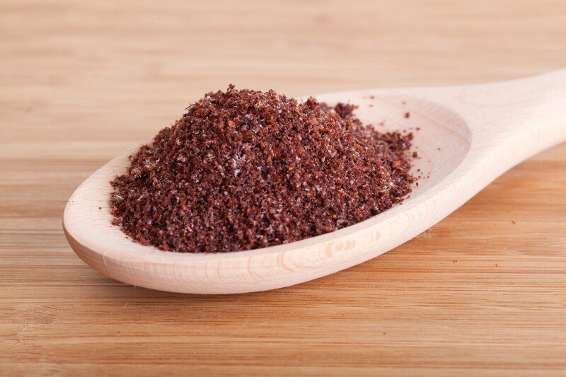 on a wooden surface is a wooden spoon full of sumac