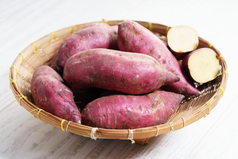 on a wooden surface is a weaved tray with sweet potatoes on it, one cut in half