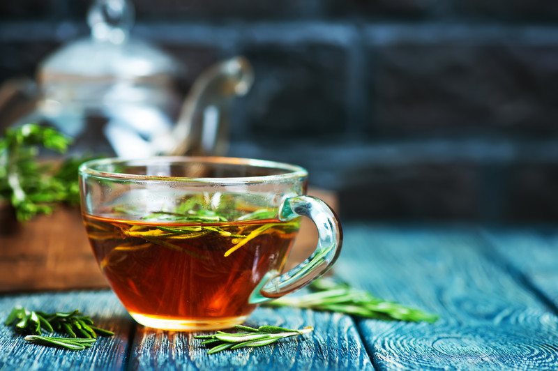 closeup image of a clear cup of tea with fresh leaves with metal teapot at the back