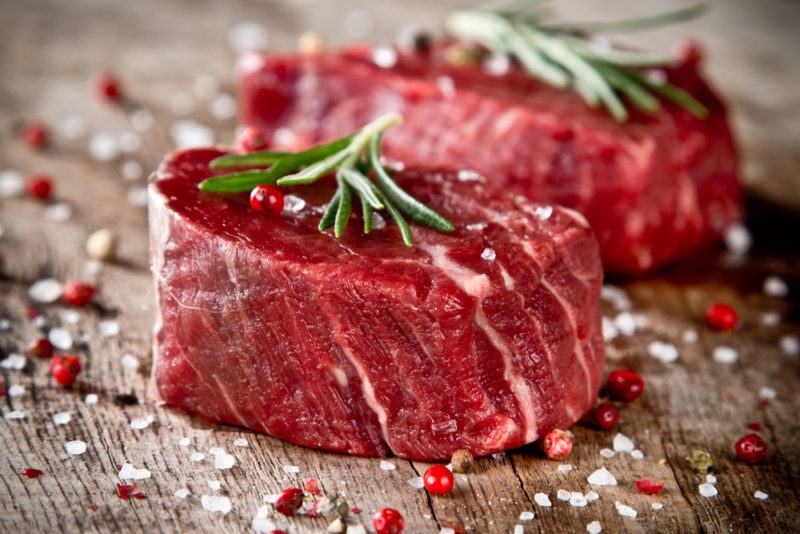 Two raw pieces of tenderloin steak with a sprig of rosemary each and plenty of salt and pepper