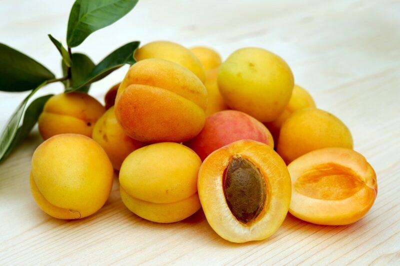 a pile of bright apricots with green stems in the corner to represent the best apricot brandy