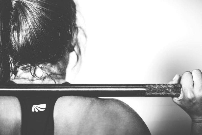 a close up of a women working out, view of behind her neck and shoulders holding a bar to represent the best protein powder for women 