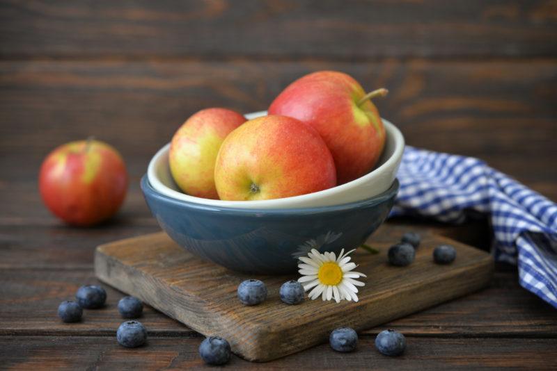 three apples on a white bowl, another apple at the background