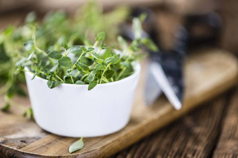 a closeup image of a white ramekin full of fresh thyme resting on a wooden chopping board with black pair of scissors at the back