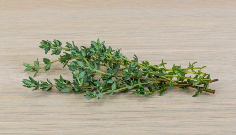 on a wooden surface is a sprig of fresh thyme