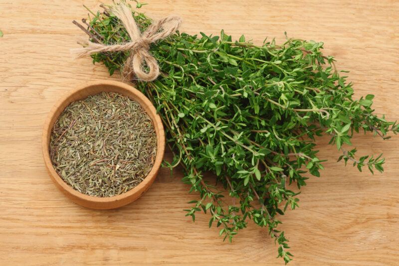 overhead shot of a wooden surface with a bunch of fresh thyme and a wooden bowl with dried thyme