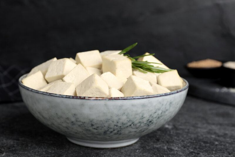 on a dark surface is a ceramic bowl with blue prints with cubed tofu with a sprig of herb on top