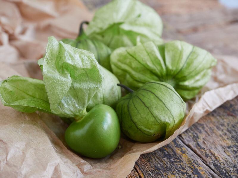 on a rustic wooden surface are tomatillos with husks resting on a brown paper