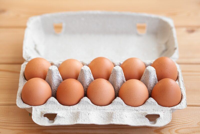 on a wooden surface is a paper carton of brown eggs