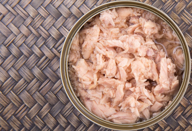 Overhead view of an open can of pink tuna against a woven brown mat background.