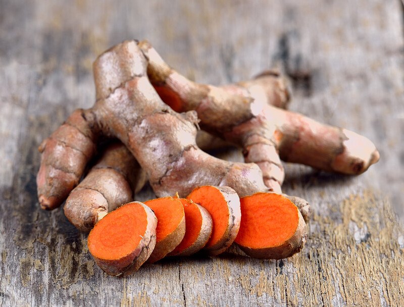 closeup image of turmeric with few sliced ones, laid out on a wooden surface