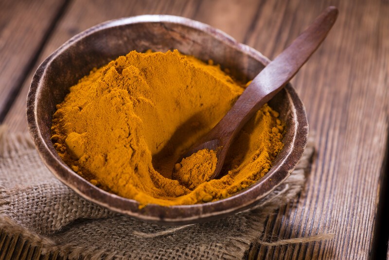 on a wooden surface is a dark brown wooden bowl with burlap underneath it with turmeric powder and wooden spoon shoved in it